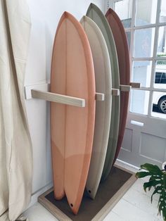 three surfboards are leaning up against the wall in front of a window with a potted plant next to it