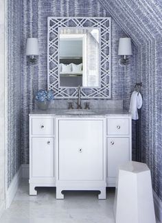 a white bathroom with blue and white wallpaper on the walls next to a mirror