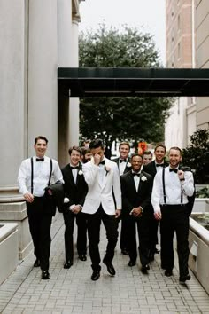 a group of men standing next to each other on a brick walkway in front of tall buildings