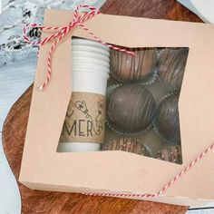 a box filled with chocolate covered donuts on top of a wooden cutting board next to a cup