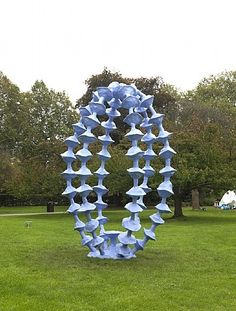 a blue sculpture in the middle of a grassy area with trees in the back ground