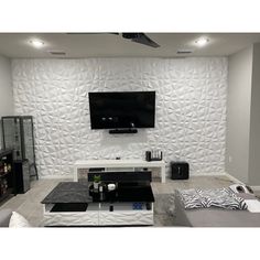 a modern living room with white walls and black furniture in the center, along with a flat screen tv mounted on the wall