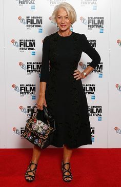 an older woman standing on a red carpet with her hands in her pockets and holding a purse