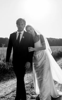 a bride and groom walking down a dirt road in front of a cornfield at sunset