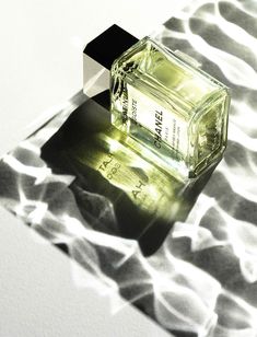 a bottle of perfume sitting on top of a white surface with light coming through it