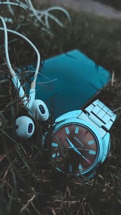 a watch and earbuds laying on the ground next to each other in some grass