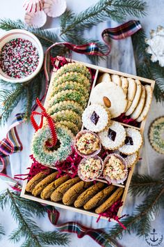 an assortment of cookies and pastries in a wooden box on a table with christmas decorations