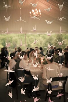 a group of people sitting around a table with paper cranes flying over them in the air