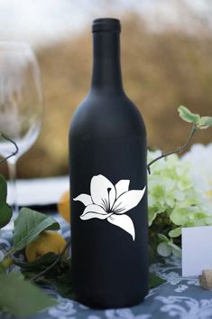 a black bottle with a white flower decal on it sitting next to some flowers