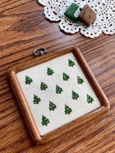 a cross stitch christmas ornament on a wooden tray next to a spool of thread