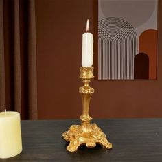 a gold candle holder sitting on top of a wooden table next to a white candle