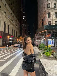 a woman is standing in the middle of an empty city street at night with her back turned to the camera