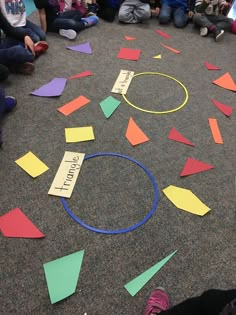 a group of children sitting on the floor in front of a circle with colored paper