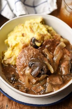 a bowl filled with meat, mushrooms and mashed potatoes on top of a wooden table