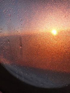 the sun is setting in the distance from an airplane window with water droplets on it