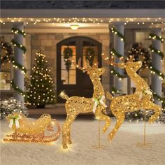 two gold reindeer statues in front of a house decorated with christmas lights and garlands