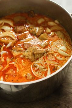 a pot filled with meat and noodles on top of a wooden table