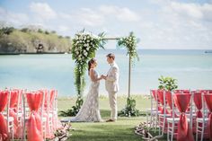 a bride and groom standing in front of an outdoor ceremony set up with red chairs