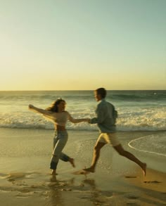 a man and woman running on the beach with waves coming in from the ocean behind them