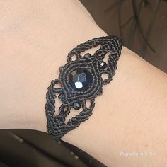 a woman's arm wearing a black bracelet with an intricate design on the wrist