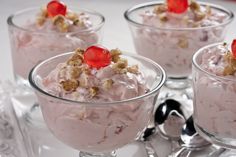 four desserts in small glass bowls with cherries on top and spoons next to them