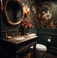 a bathroom with floral wallpaper and gold fixtures on the vanity, along with a white toilet