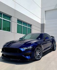 a blue mustang parked in front of a building with garage doors and windows on the side