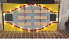 a lighted board with some notes pinned to it and string lights on the sides, in front of a fireplace