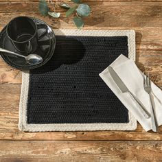 a place mat with silverware and a black cup on it next to a white napkin