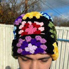 a man wearing a multicolored crocheted hat with flowers on the front