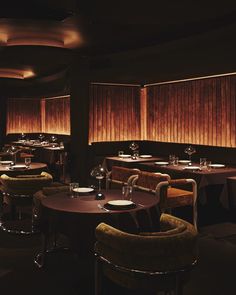 a dimly lit dining room with round tables and velvet upholstered chairs in the center