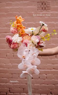 a person holding a bouquet of flowers in front of a brick wall with words above it