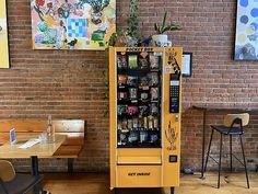 a vending machine sitting in front of a brick wall next to a wooden table