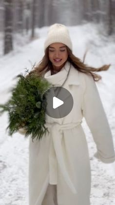 a woman is walking in the snow with a wreath around her neck and wearing a white coat