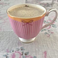 a pink and white striped coffee cup sitting on top of a floral tablecloth covered table