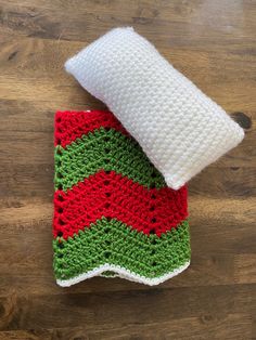 two crocheted dishcloths sitting on top of a wooden table next to a white pillow