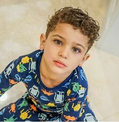 a young boy sitting on the floor wearing pajamas and looking up at the camera with his hands in his pockets