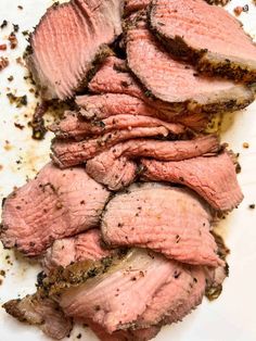 sliced meat sitting on top of a white plate next to seasoning and pepper flakes