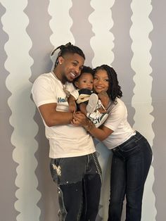 a man and woman holding a baby in front of a wall with wavy designs on it