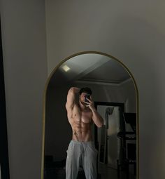 a shirtless man taking a selfie in front of a mirror with his cell phone