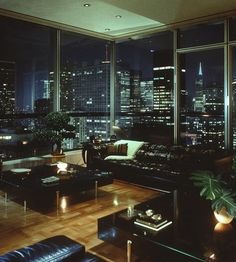 a living room filled with lots of furniture and tall buildings in the background at night