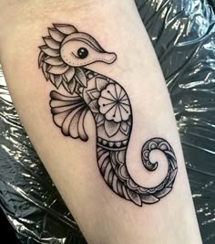 a black and white photo of a seahorse tattoo on the leg, with flowers around it