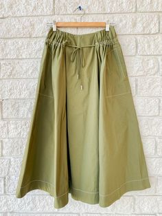 Simkhai Tona Midi Skirt in Army Green Midi length High waisted Adjustable waist tie Oversized patch pocket Khaki Midi Skirt For Spring, Khaki Flowy Skirt For Spring, Green Midi Bottoms With Elastic Waistband, Mother Denim, Knit Sweatshirt, Frame Denim, Outerwear Sweater, Ulla Johnson, Designer Outfits Woman