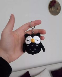 a hand holding an owl keychain in front of a white wall