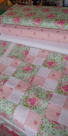 pink and green quilting on top of a bed with white polka dot sheets in the background