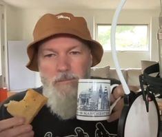 a man with a beard holding a coffee cup and cracker in front of his face