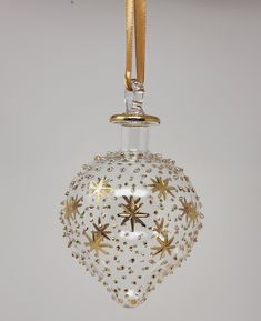 a glass ornament hanging from a gold - colored cord on a white wall