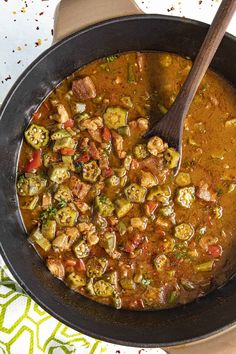 a pan filled with stew and vegetables on top of a table next to a wooden spoon