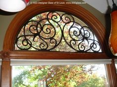 an arched window with decorative iron work on the top and bottom, in front of a tree