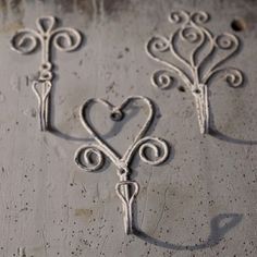 three wrought iron heart and key hooks on a concrete wall with the shadow of a person